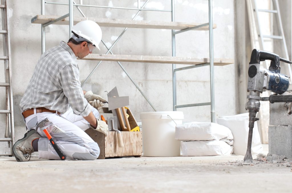 plasterer man construction worker work with tool box wear gloves, hard hat and protection glasses at interior building site with scaffolding. bucket, sacks and jackhammer